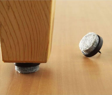 A gray wool felt nail is installed on the table leg and two another wool felt nails on the floor.