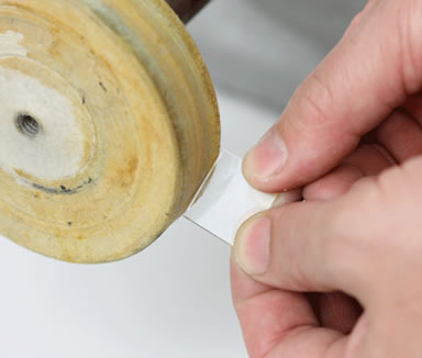 A hand is polishing a piece of glass on wool felt polishing wheel.
