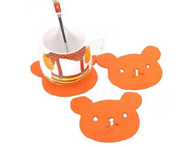 Three orange bear shaped wool felt coasters with a cup and a spoon on the one coaster.