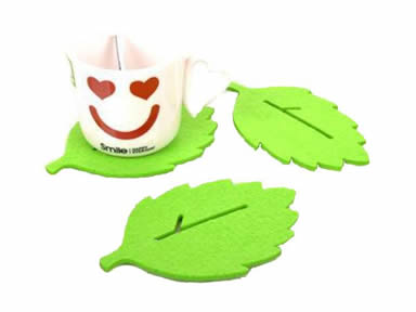 Three green leaf shaped wool felt coasters with a cup and a spoon on the one coaster.