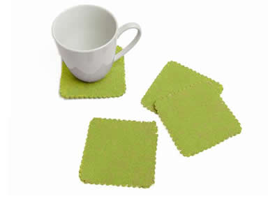 Four green coasters on the white table and a white cup on one coaster.